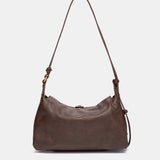 Schultertasche mit braunem Quasten-Anhänger.